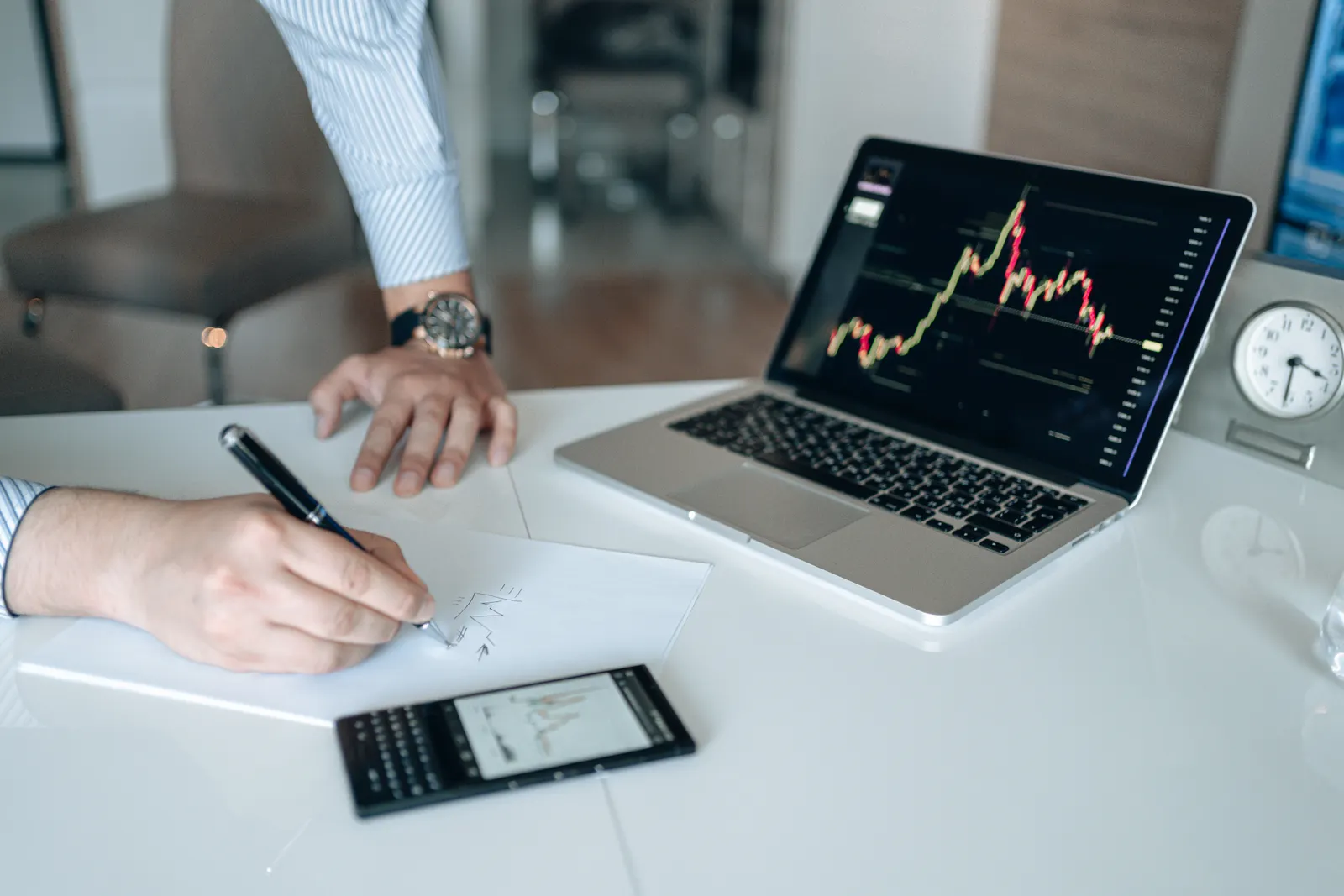 Profesional tomando notas mientras revisa información financiera en una computadora